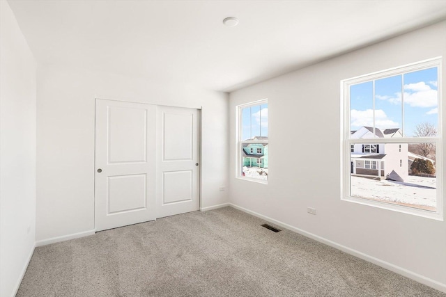 unfurnished bedroom with a closet, light colored carpet, visible vents, and baseboards