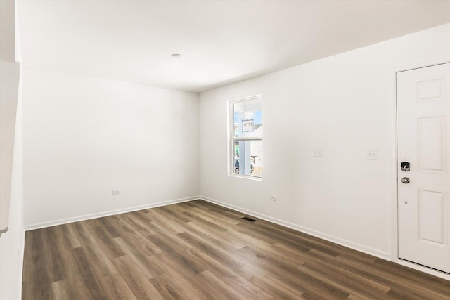 spare room featuring dark wood-style flooring, visible vents, and baseboards