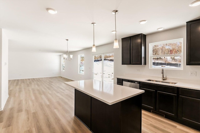 kitchen with light wood finished floors, a center island, hanging light fixtures, light countertops, and a sink