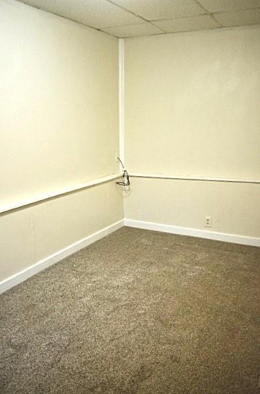 empty room with dark colored carpet and a drop ceiling