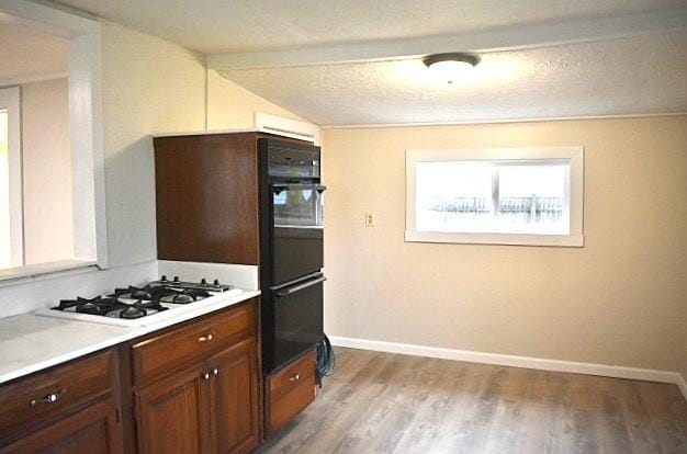 kitchen with lofted ceiling, light wood-type flooring, white gas stovetop, and a textured ceiling