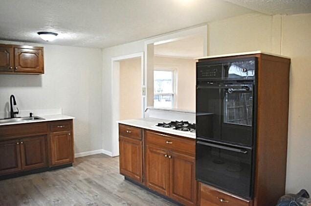 kitchen featuring a textured ceiling, sink, light hardwood / wood-style flooring, and white gas stovetop