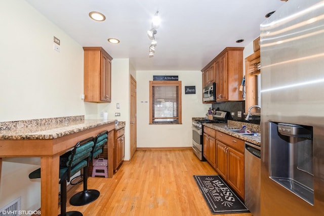 kitchen with stone countertops, light hardwood / wood-style floors, sink, and stainless steel appliances