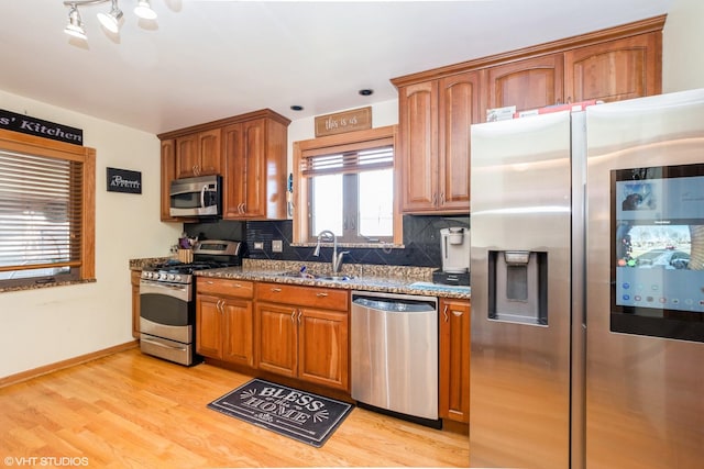 kitchen with tasteful backsplash, stainless steel appliances, sink, stone countertops, and light hardwood / wood-style flooring