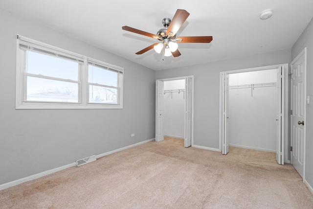 unfurnished bedroom featuring ceiling fan, light carpet, and two closets