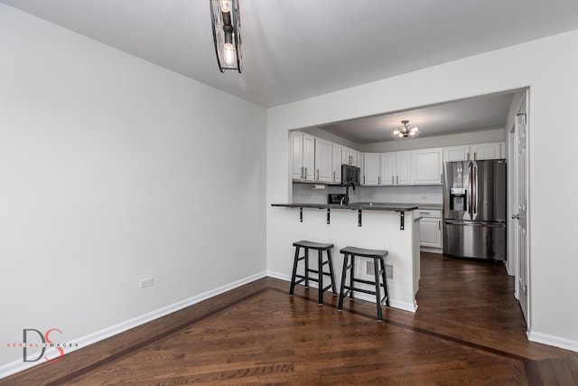 kitchen featuring kitchen peninsula, stainless steel refrigerator with ice dispenser, backsplash, a kitchen breakfast bar, and white cabinetry