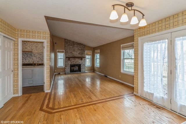 unfurnished living room with vaulted ceiling, a brick fireplace, hardwood / wood-style floors, and washing machine and dryer