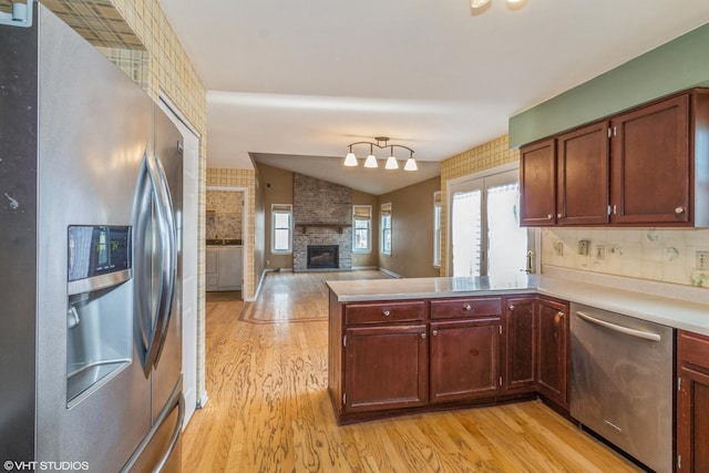 kitchen with vaulted ceiling, light wood-type flooring, appliances with stainless steel finishes, kitchen peninsula, and a fireplace