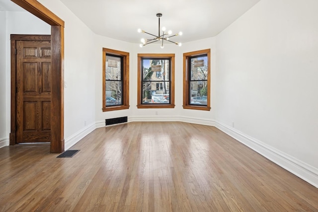 empty room with a chandelier, hardwood / wood-style flooring, and a healthy amount of sunlight