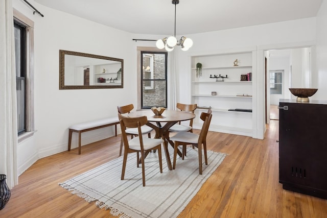 dining area featuring built in shelves, light hardwood / wood-style flooring, and a notable chandelier