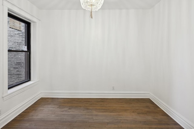 spare room with dark wood-type flooring and a notable chandelier