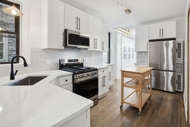 kitchen with appliances with stainless steel finishes, white cabinetry, hanging light fixtures, and sink