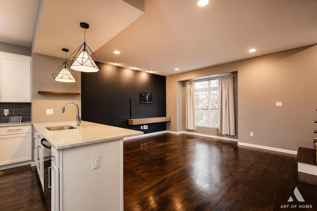 kitchen with light stone counters, white cabinetry, sink, and hanging light fixtures