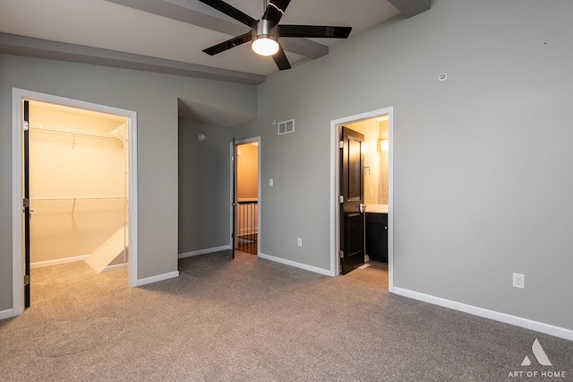 unfurnished bedroom with a walk in closet, connected bathroom, light colored carpet, vaulted ceiling with beams, and a closet