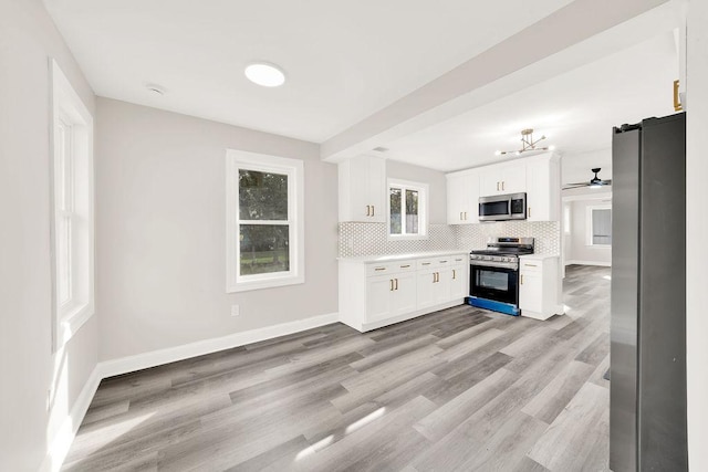 kitchen with backsplash, white cabinets, ceiling fan, appliances with stainless steel finishes, and light hardwood / wood-style floors