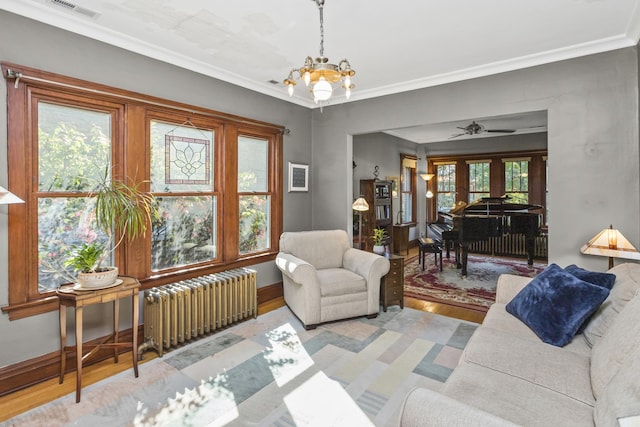 living area with ceiling fan with notable chandelier, radiator heating unit, crown molding, and light hardwood / wood-style flooring