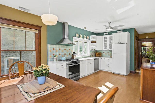 kitchen with decorative light fixtures, stainless steel appliances, white cabinetry, and wall chimney range hood