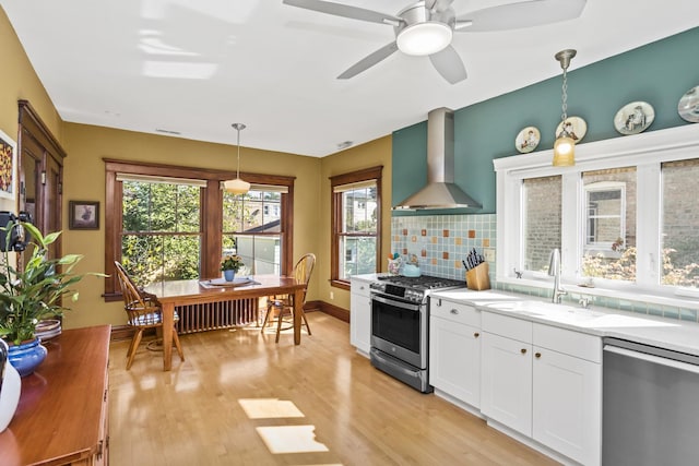 kitchen with pendant lighting, white cabinets, wall chimney range hood, sink, and appliances with stainless steel finishes