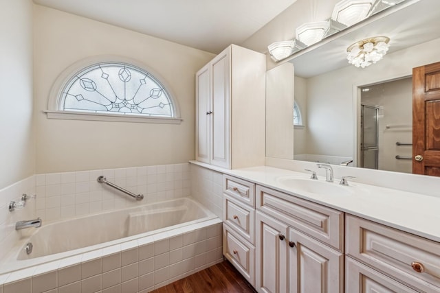 bathroom featuring wood-type flooring, vanity, a healthy amount of sunlight, and tiled tub