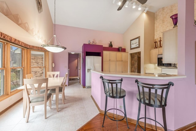 kitchen with high vaulted ceiling, white refrigerator with ice dispenser, kitchen peninsula, decorative light fixtures, and a breakfast bar