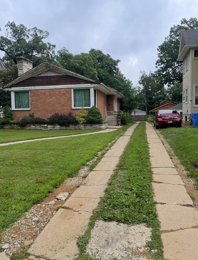 view of side of property with a yard, brick siding, driveway, and a chimney