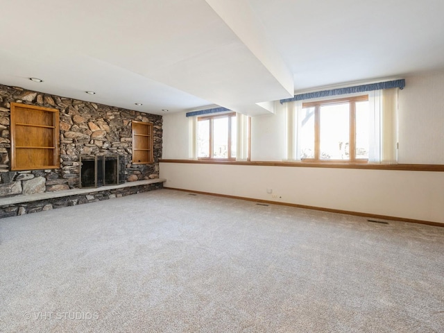 unfurnished living room featuring plenty of natural light, a stone fireplace, and carpet flooring