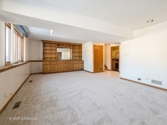 unfurnished living room featuring light carpet and built in shelves