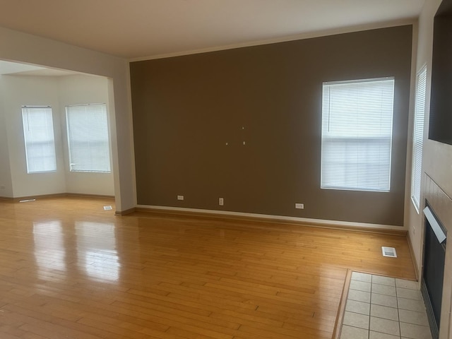 empty room featuring a healthy amount of sunlight, a tiled fireplace, and light wood-type flooring