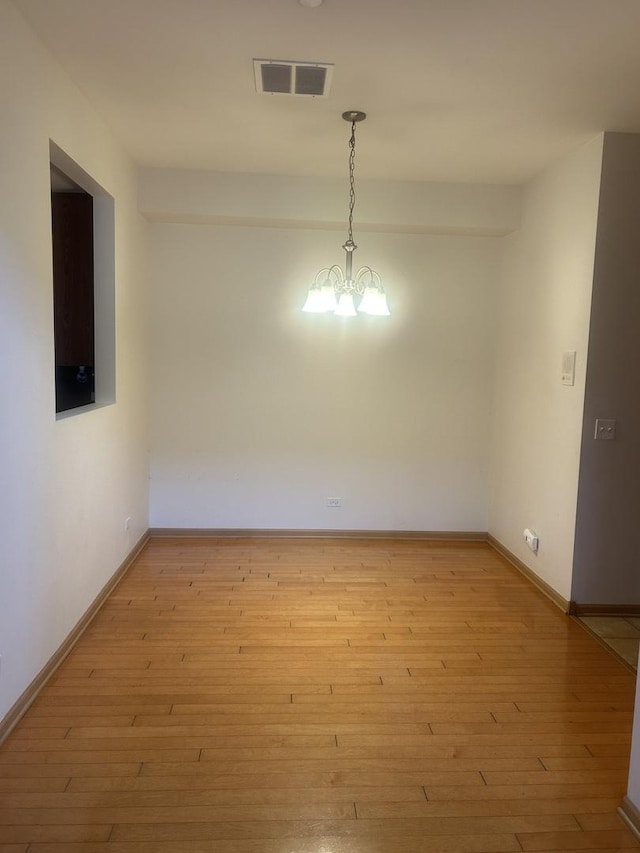 empty room with light wood-type flooring and a chandelier