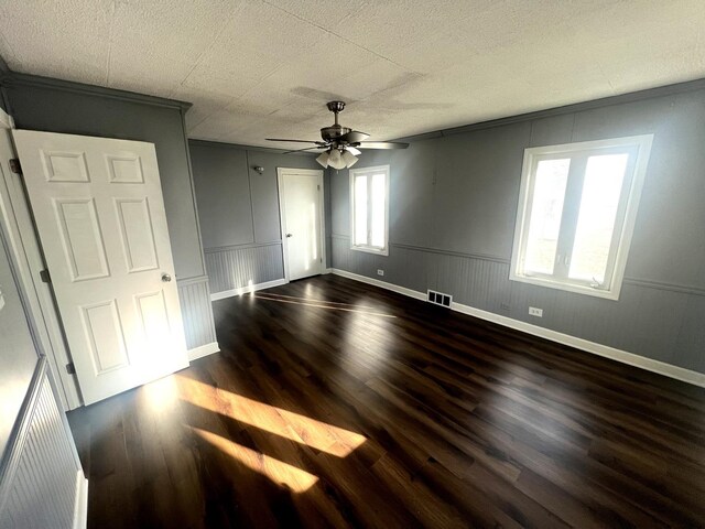 unfurnished bedroom with visible vents, baseboards, a wainscoted wall, ceiling fan, and dark wood-style flooring