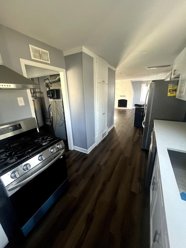 kitchen with dark wood-style floors, stainless steel gas range oven, visible vents, and white cabinetry