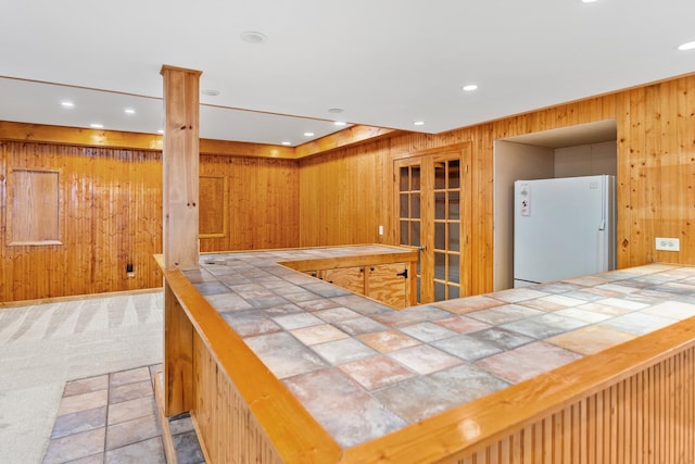 kitchen with white fridge, tile counters, and wood walls