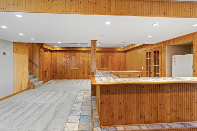 kitchen featuring tile counters, white refrigerator, kitchen peninsula, wood walls, and light colored carpet