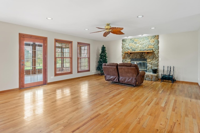 living room featuring light hardwood / wood-style floors, a stone fireplace, and ceiling fan