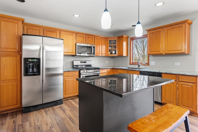 kitchen featuring hanging light fixtures, stainless steel appliances, light hardwood / wood-style flooring, dark stone countertops, and a kitchen island