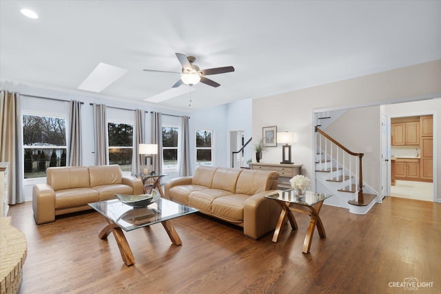 living room with ceiling fan, a skylight, and hardwood / wood-style flooring