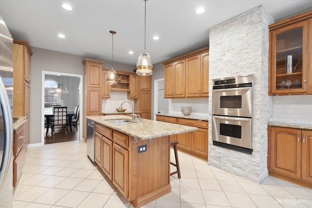 kitchen with light stone counters, tasteful backsplash, a kitchen island with sink, appliances with stainless steel finishes, and sink