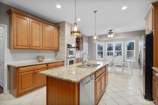 kitchen with a center island with sink, appliances with stainless steel finishes, ceiling fan, sink, and tasteful backsplash