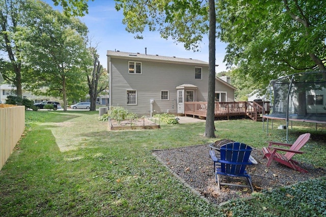 back of property featuring a lawn, a wooden deck, and a trampoline