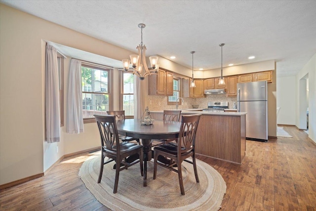 dining room featuring a textured ceiling, sink, a notable chandelier, and light wood-type flooring