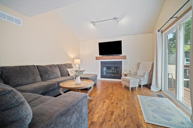 living room with wood walls, rail lighting, lofted ceiling, and hardwood / wood-style flooring