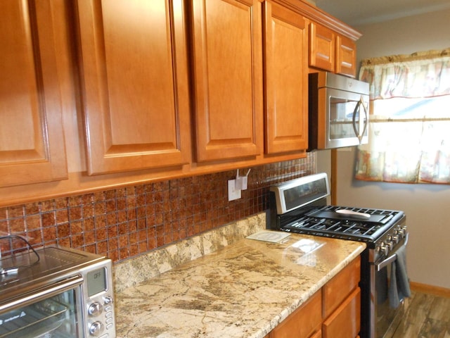 kitchen featuring backsplash, light stone counters, hardwood / wood-style floors, and appliances with stainless steel finishes