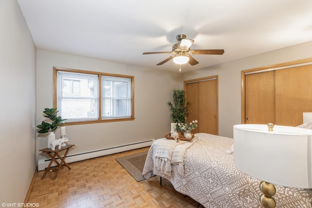 bedroom with light parquet flooring, a baseboard radiator, ceiling fan, and multiple closets