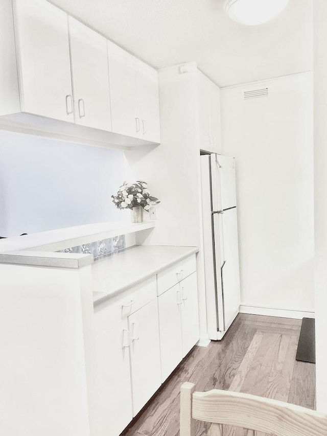 kitchen with white cabinetry, white fridge, and light hardwood / wood-style floors