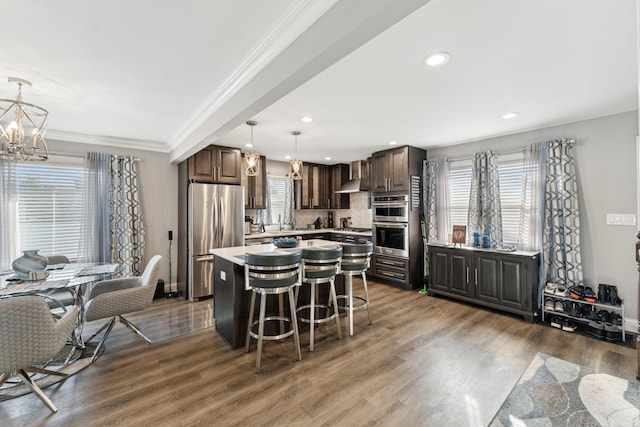 kitchen featuring pendant lighting, a center island, wall chimney exhaust hood, appliances with stainless steel finishes, and a breakfast bar area