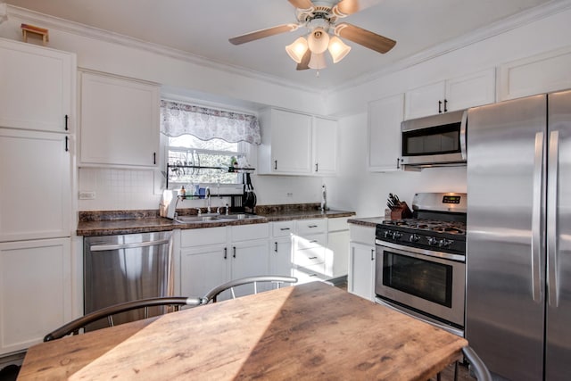 kitchen featuring sink, white cabinetry, stainless steel appliances, ornamental molding, and dark stone counters