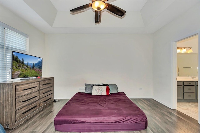 bedroom featuring hardwood / wood-style floors, ensuite bathroom, a raised ceiling, and ceiling fan