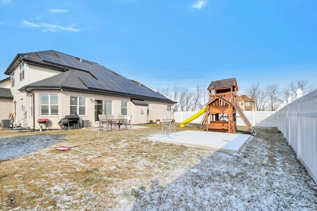 back of house with a patio area, a playground, a fenced backyard, and roof mounted solar panels