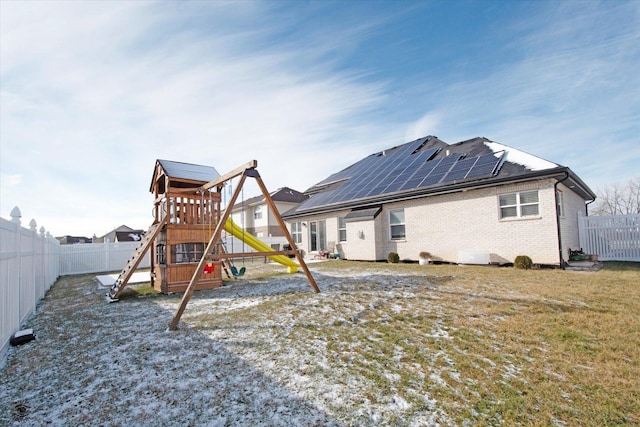 rear view of property featuring a playground, brick siding, a fenced backyard, and solar panels