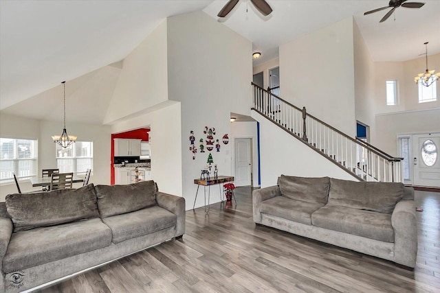 living area featuring high vaulted ceiling, ceiling fan with notable chandelier, stairway, and wood finished floors